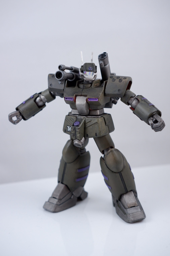 The Guncannon Mass Production Type is a bulky, heavily-armored bipedal mobile suit with two large cannons mounted on its back for medium-range fire support. This particular unit is painted with German grey armor with purple accents over a metallic iron endoskeleton.