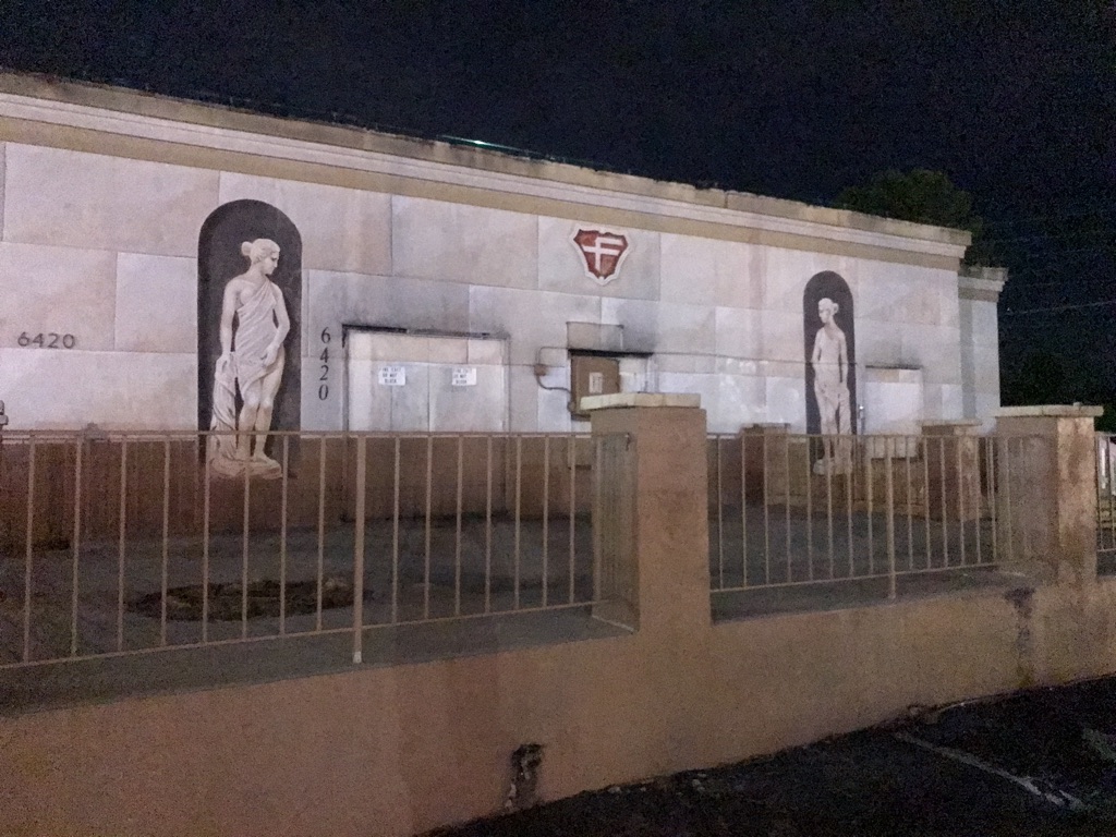 A stone slab building painted to look like it’s made of marble and has eaves housing neoclassical statuary in the Grecian style. Completely abandoned.