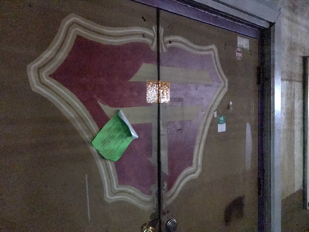 The front door has been duct-taped shut and a peeling green notice is haphazardly stuck upside-down on the door.