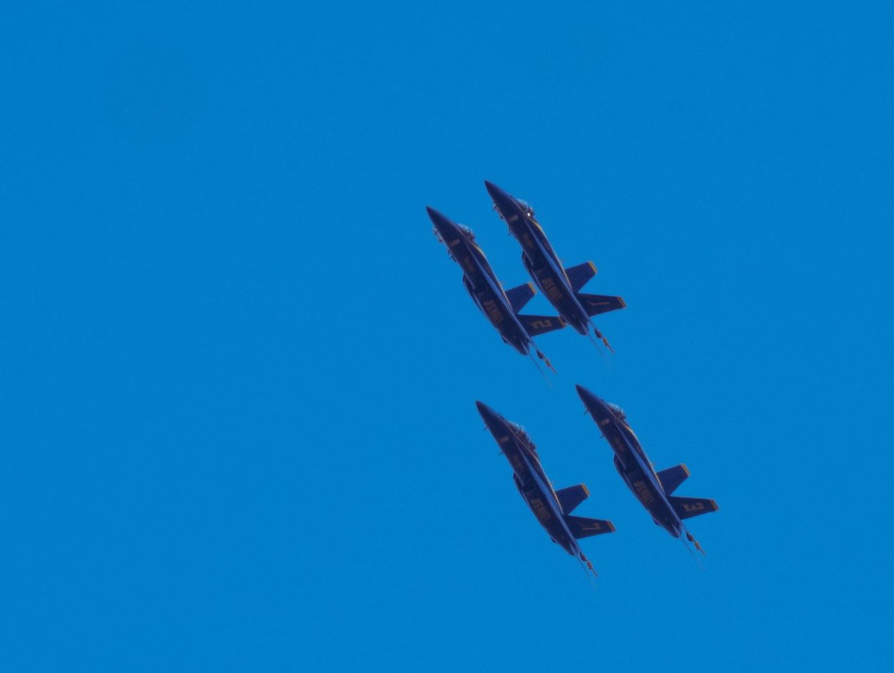 Four Blue Angels jets in a tight diamond formation haul ass through the sky.