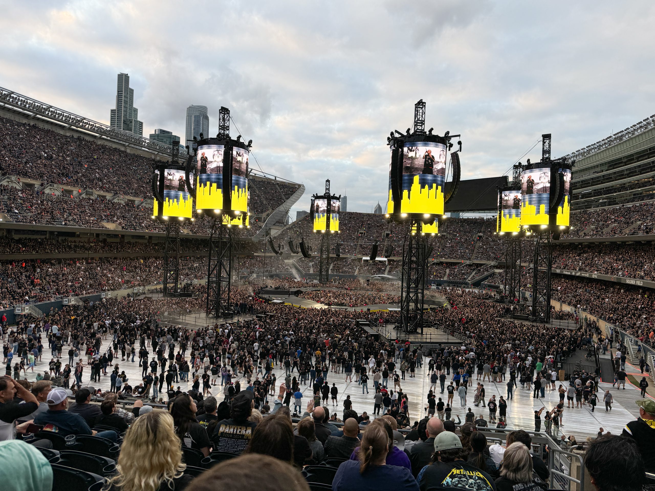 Soldier Field, set up for a concert. Eight speaker towers with video screens circle a raised stage set up in the round, with a section in the middle of the stage for VIP guests.