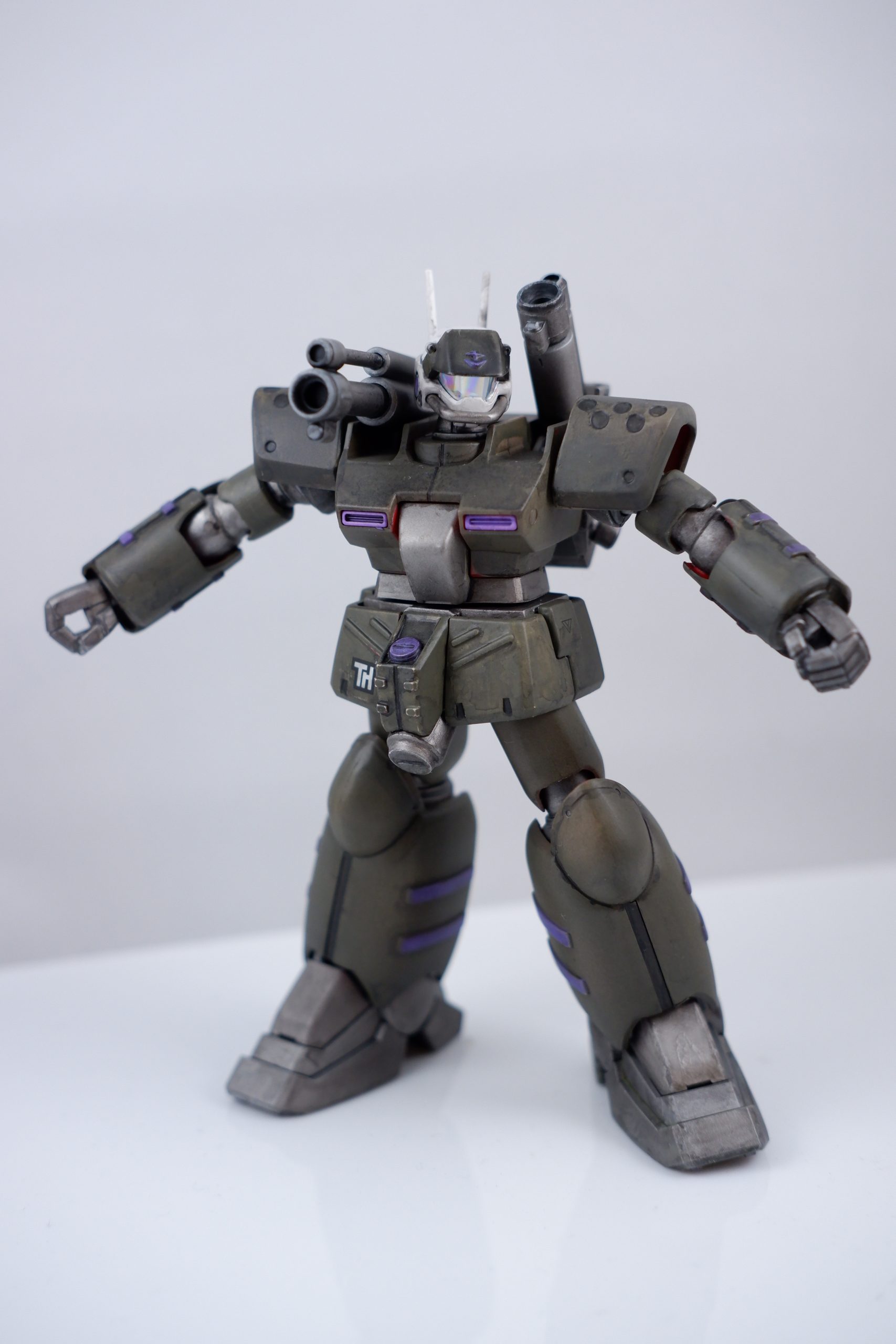 This is a close up photograph of a customized model kit, specifically the 1/144 Guncannon Mass Production Type from Mobile Suit Gundam 0080: War in the Pocket. The model is painted in German gray, gunmetal, and purple for that slightly weird toyetic ’80s flavor. 