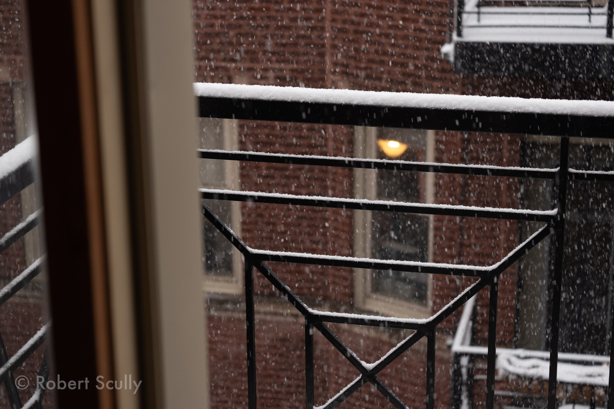 A view of my porch from inside. About an inch of snow is balanced on the porch railing.