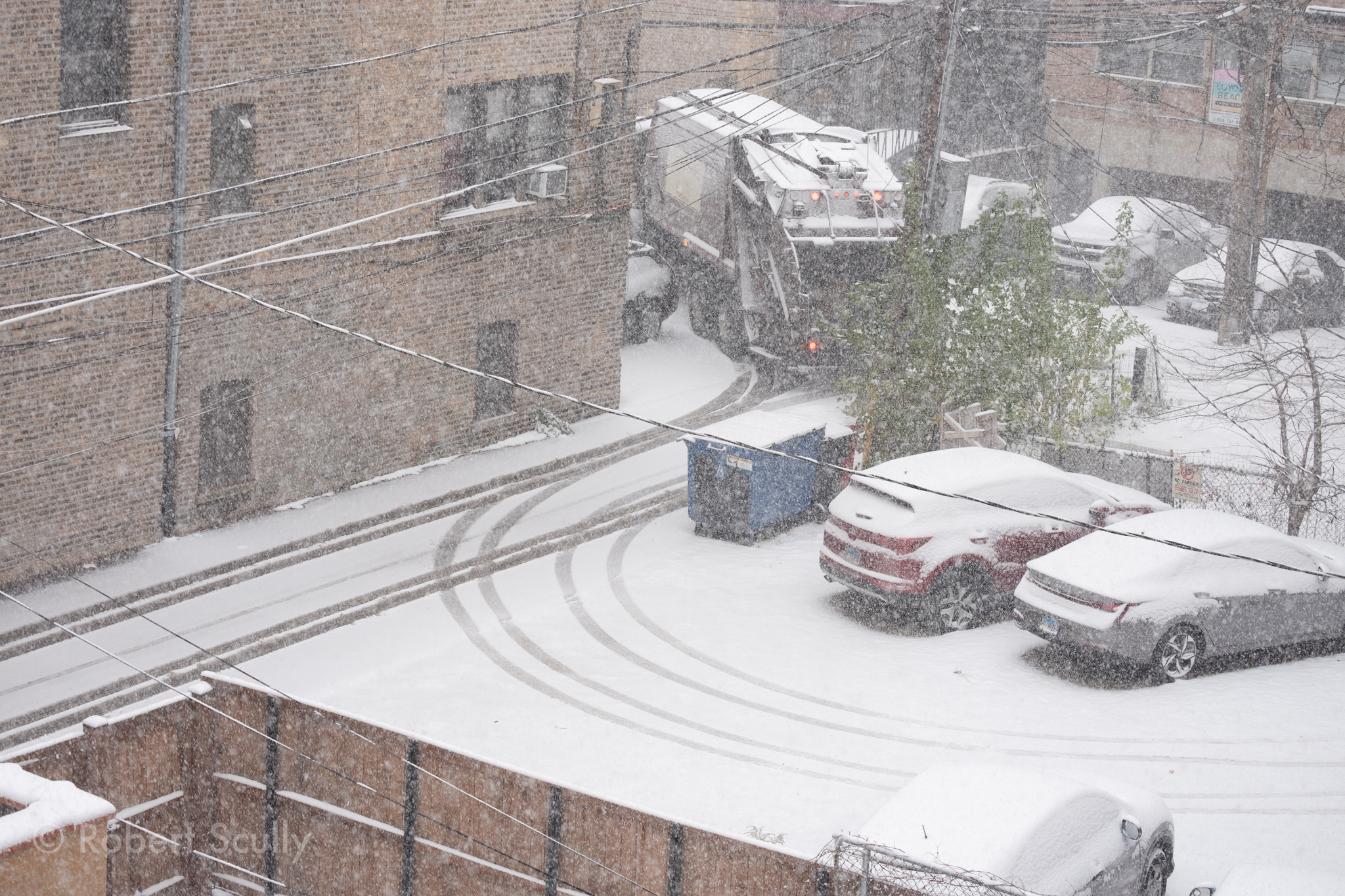 The parking lot behind my building. We see a garbage truck pulling away, through an overlay of tangled power cables covered in snow.